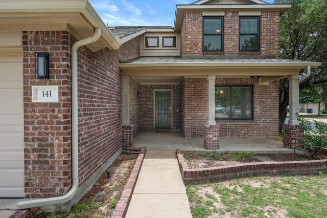 property entrance featuring brick siding, covered porch, and roof with shingles