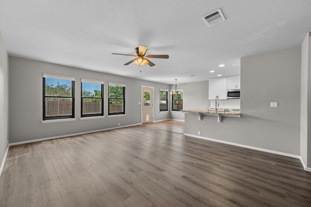 unfurnished living room with ceiling fan, wood finished floors, baseboards, recessed lighting, and a chandelier