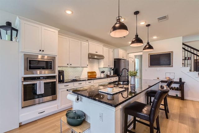 206 Monteforte Rd, Hutto, TX 78634 - kitchen featuring stainless steel appliances, a kitchen breakfast bar, light wood-type flooring, an island with sink, and backsplash