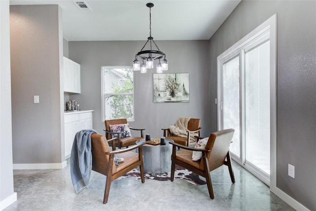 living area with concrete flooring, a chandelier, and baseboards