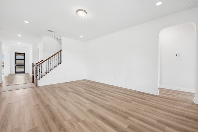 unfurnished living room featuring stairway, arched walkways, light wood-type flooring, baseboards, and recessed lighting