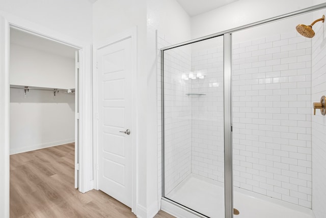 full bath featuring a shower stall, wood finished floors, and a walk in closet