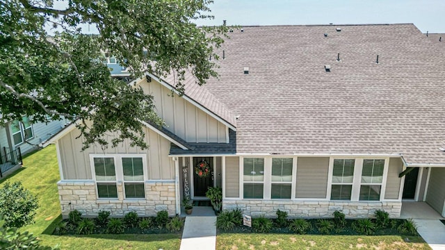view of front of home featuring stone siding, board and batten siding, roof with shingles, and a front yard