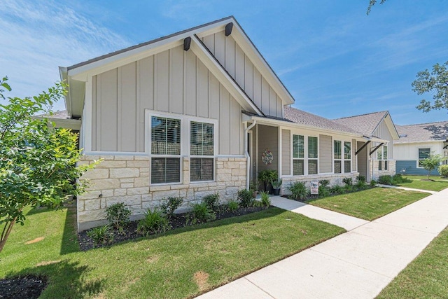 view of front facade with board and batten siding, stone siding, and a front yard