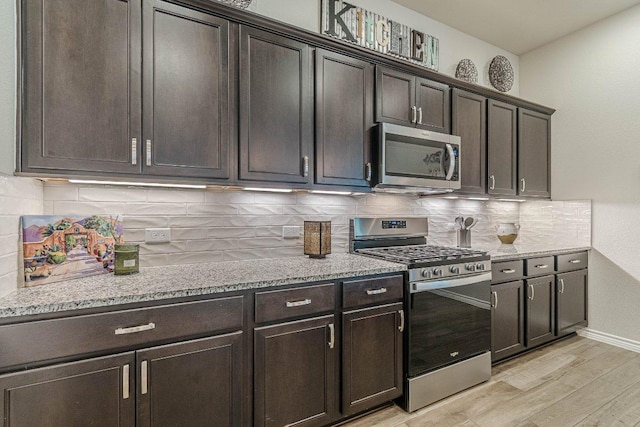 kitchen with stainless steel appliances, light wood-style floors, light stone counters, tasteful backsplash, and dark brown cabinets