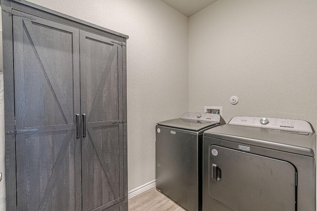washroom with washing machine and dryer, cabinet space, light wood-style floors, baseboards, and a textured wall