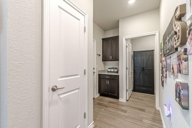 corridor featuring light wood finished floors, a textured wall, and baseboards