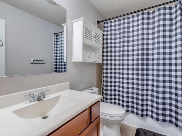 bathroom with toilet, vanity, and a textured wall
