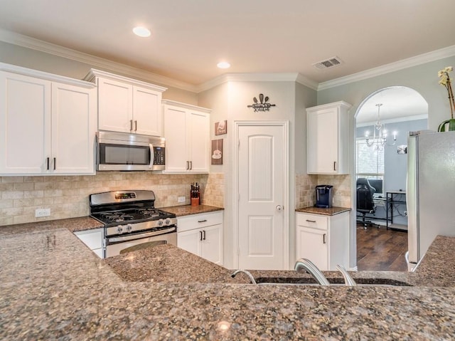 kitchen featuring appliances with stainless steel finishes, arched walkways, white cabinetry, a chandelier, and dark stone counters