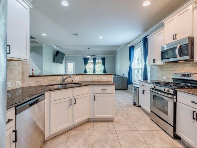 kitchen with appliances with stainless steel finishes, a sink, ceiling fan, backsplash, and dark stone countertops