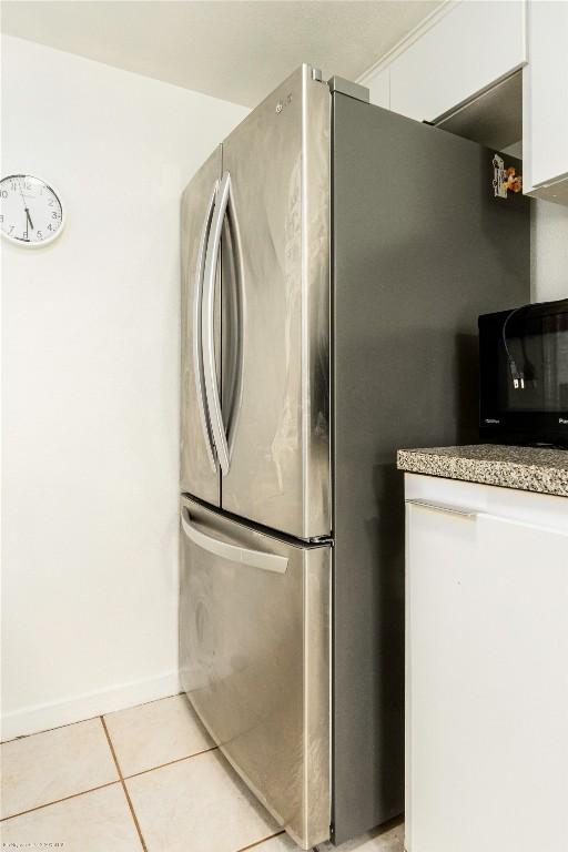 5601 Woodrow Ave Unit 109, Austin, TX 78756 - kitchen featuring freestanding refrigerator, black microwave, light tile patterned flooring, baseboards, and white cabinetry