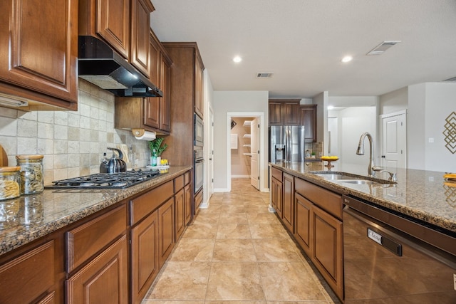 kitchen with appliances with stainless steel finishes, a sink, dark stone counters, backsplash, and recessed lighting