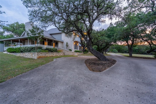 view of front facade featuring a standing seam roof, curved driveway, a chimney, metal roof, and covered porch