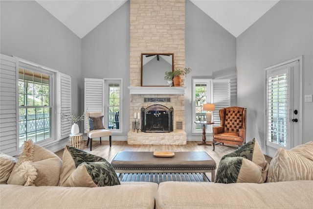 living room featuring high vaulted ceiling, a stone fireplace, and wood finished floors