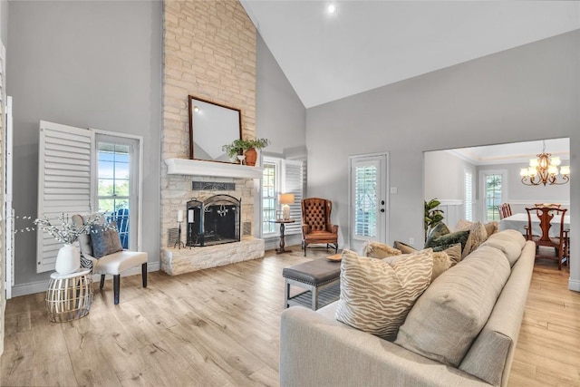 living area featuring high vaulted ceiling, a fireplace, a chandelier, light wood-type flooring, and baseboards