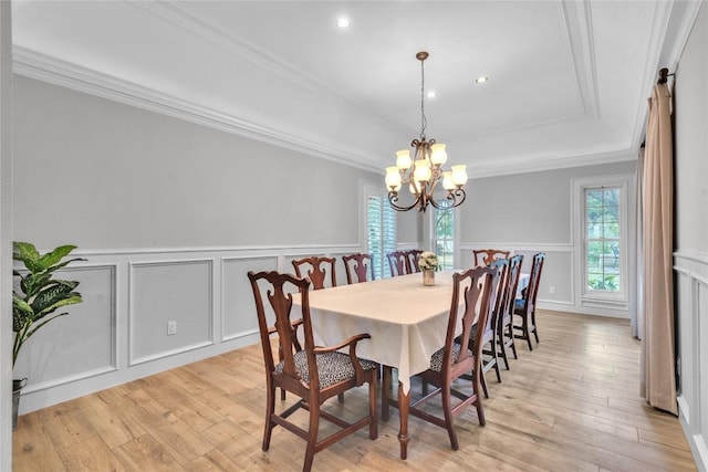 dining space with a decorative wall, a chandelier, a raised ceiling, ornamental molding, and light wood-type flooring
