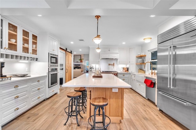 kitchen featuring built in appliances, a barn door, white cabinets, light wood-style floors, and recessed lighting