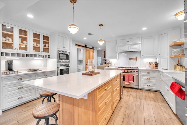 kitchen featuring appliances with stainless steel finishes, a barn door, light wood-style floors, light countertops, and recessed lighting