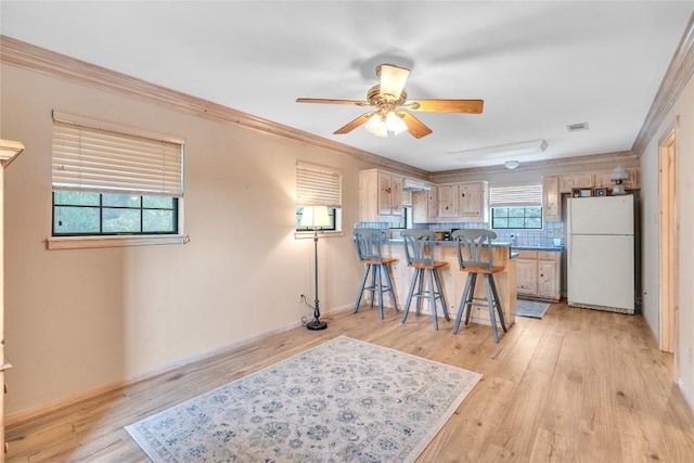 kitchen with freestanding refrigerator, a ceiling fan, a breakfast bar area, light wood finished floors, and ornamental molding