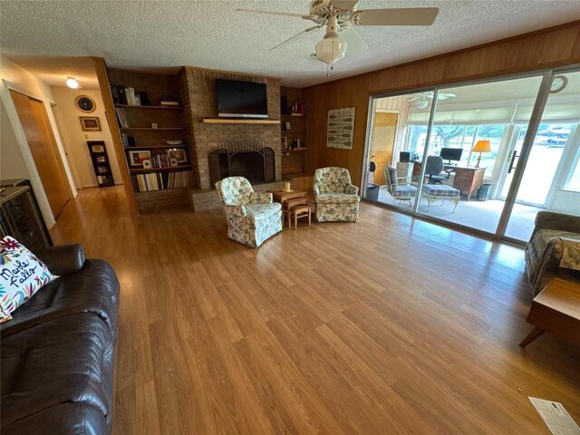 304 E Pheasant Rd, Highland Haven, TX 78654 - living area with a textured ceiling, a brick fireplace, a ceiling fan, wood finished floors, and wooden walls