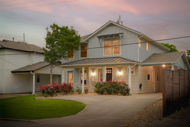 view of front of house featuring a porch, a standing seam roof, concrete driveway, metal roof, and a lawn