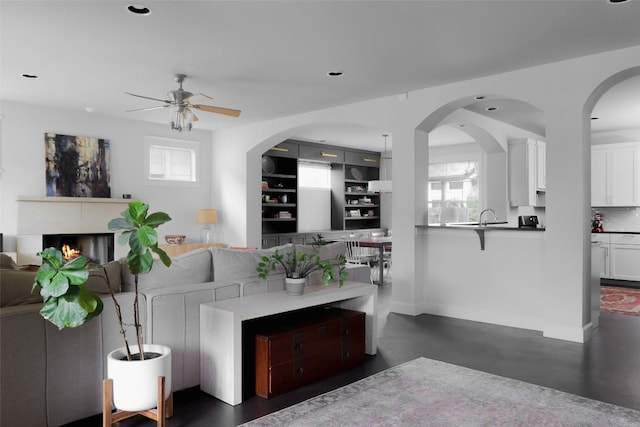 living area with a ceiling fan, a lit fireplace, recessed lighting, baseboards, and concrete flooring