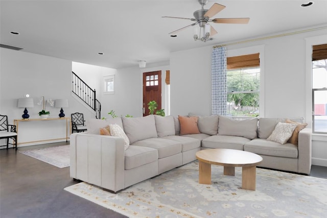 living area featuring stairway, ceiling fan, and concrete floors
