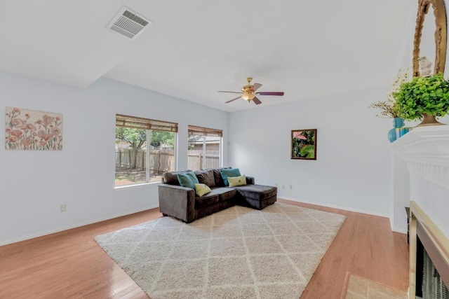 living room with a fireplace with flush hearth, light wood-style floors, a ceiling fan, and baseboards