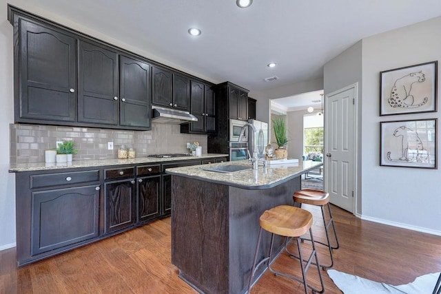 3831 Epperson Trl, Austin, TX 78732 - kitchen with baseboards, wood finished floors, a kitchen bar, appliances with stainless steel finishes, and backsplash