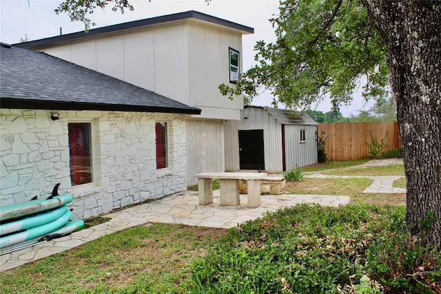 24701 Martin Ln, Spicewood, TX 78669 - rear view of house featuring a shingled roof, stone siding, a storage shed, and a patio