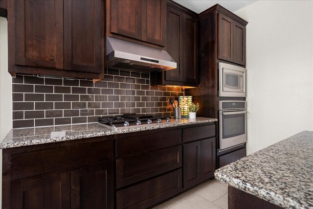 5517 Brady Bayou Cv, Austin, TX 78738 - kitchen with appliances with stainless steel finishes, under cabinet range hood, decorative backsplash, dark brown cabinetry, and light stone counters