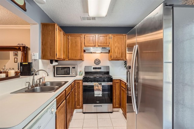 kitchen with appliances with stainless steel finishes, under cabinet range hood, a sink, light tile patterned floors, and a textured ceiling