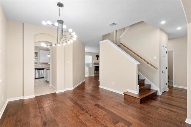 2502 Nightshade Dr, Cedar Park, TX 78613 - unfurnished living room featuring arched walkways, wood finished floors, stairway, a fireplace, and a chandelier