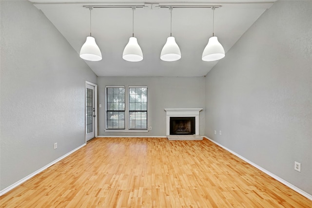 1202 Thorpe Ln Unit 508, San Marcos, TX 78666 - unfurnished living room featuring wood finished floors, baseboards, a fireplace with raised hearth, vaulted ceiling, and track lighting