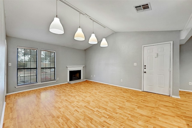 1202 Thorpe Ln Unit 508, San Marcos, TX 78666 - unfurnished living room with light wood-style flooring, vaulted ceiling, baseboards, a fireplace with raised hearth, and rail lighting