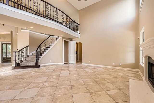 205 Sebastians Run, Austin, TX 78738 - unfurnished living room featuring a high ceiling, arched walkways, stairs, a fireplace with raised hearth, and tile patterned floors