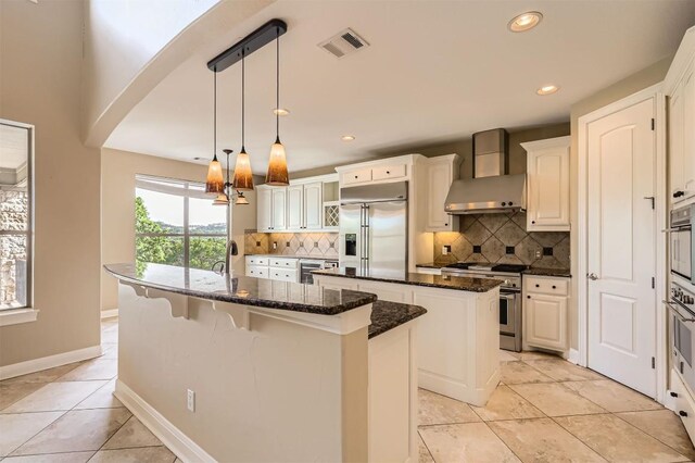 205 Sebastians Run, Austin, TX 78738 - kitchen with high end appliances, an island with sink, wall chimney range hood, tasteful backsplash, and recessed lighting