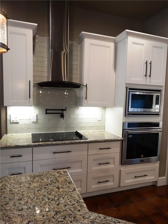 20601 Branding Iron, Lago Vista, TX 78645 - kitchen featuring stainless steel appliances, wall chimney range hood, white cabinets, light stone counters, and tasteful backsplash