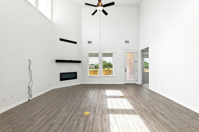 unfurnished living room featuring a ceiling fan, wood finished floors, a towering ceiling, a glass covered fireplace, and baseboards