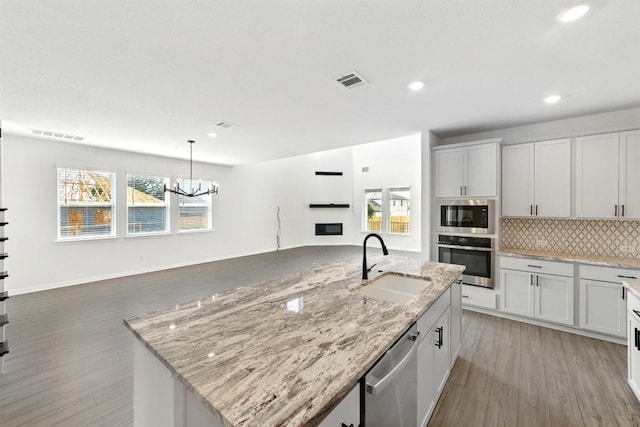 kitchen featuring stainless steel appliances, a sink, open floor plan, light wood-style floors, and recessed lighting