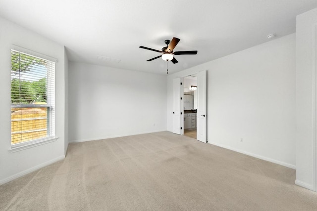 spare room featuring light colored carpet, ceiling fan, and baseboards