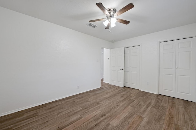 unfurnished bedroom featuring two closets, wood finished floors, baseboards, and ceiling fan