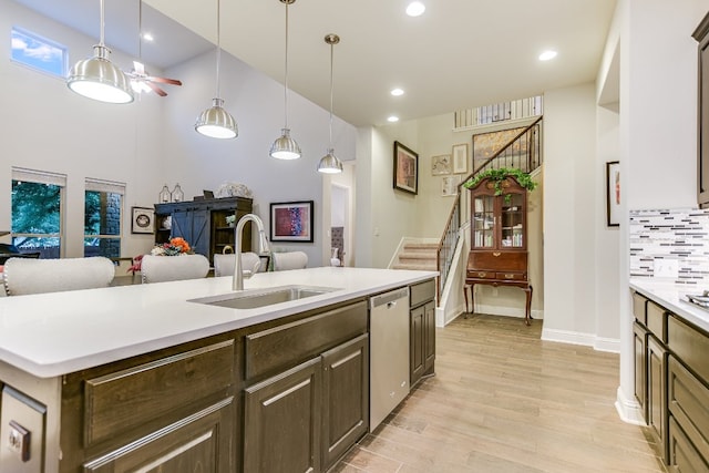 kitchen featuring a sink, dishwasher, light countertops, light wood-style floors, and an island with sink