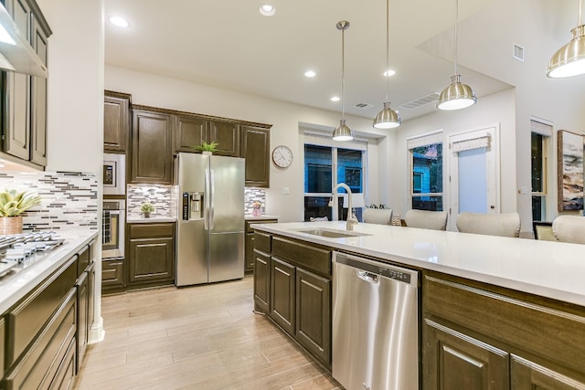 kitchen featuring appliances with stainless steel finishes, a sink, light countertops, tasteful backsplash, and light wood-style floors