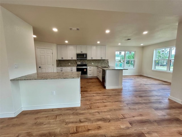 1127 Greenhill Dr, Canyon Lake, TX 78133 - kitchen with stainless steel appliances, a peninsula, light stone countertops, white cabinets, and light wood-style flooring