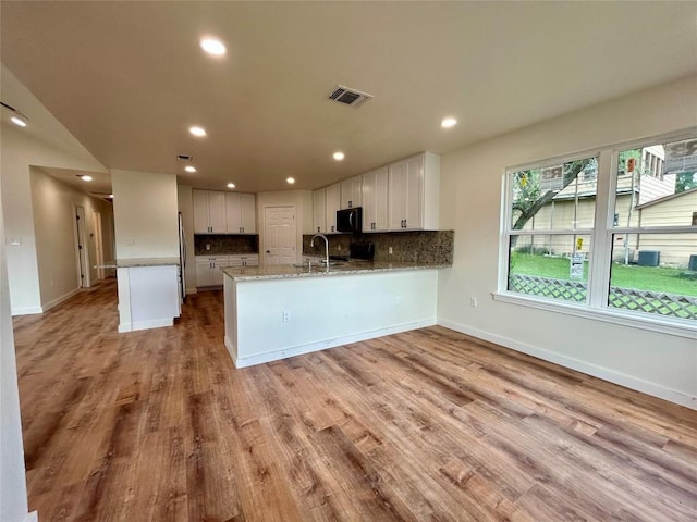 1127 Greenhill Dr, Canyon Lake, TX 78133 - kitchen featuring a peninsula, tasteful backsplash, white cabinets, light stone counters, and light wood-type flooring