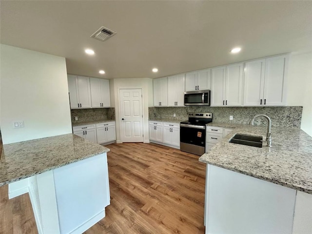 1127 Greenhill Dr, Canyon Lake, TX 78133 - kitchen with appliances with stainless steel finishes, a peninsula, light wood-type flooring, white cabinets, and light stone countertops