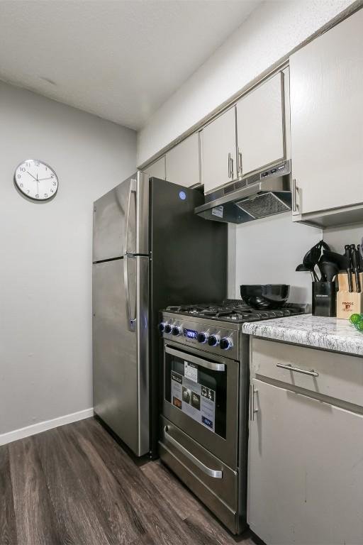 101 E 33rd St Unit 107, Austin, TX 78705 - kitchen with under cabinet range hood, stainless steel gas stove, dark wood-style floors, light countertops, and white cabinets