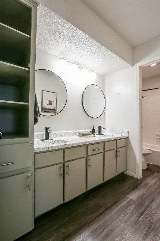 101 E 33rd St Unit 107, Austin, TX 78705 - bathroom featuring double vanity, wood finished floors, toilet, a textured ceiling, and baseboards
