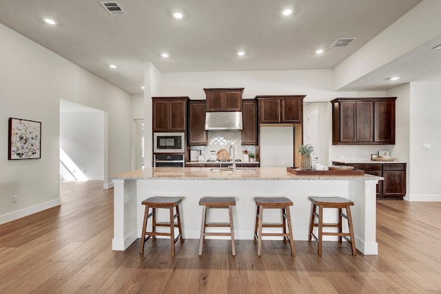 991 Arrowhead Ranch Blvd, Dripping Springs, TX 78620 - kitchen with built in microwave, stainless steel oven, under cabinet range hood, a large island, and wood finished floors